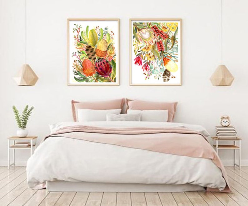 Puede incluir: Dos pinturas de acuarela enmarcadas de flores nativas australianas coloridas, que incluyen tonos rojos, amarillos y verdes, que se muestran en una pared blanca sobre una cama con ropa de cama rosa.
