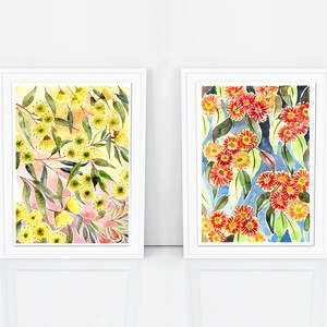 以下が含まれることがあります： 花柄のウォーターカラーの絵画が2つ額装されています。左の絵は、ピンクと黄色の背景に、緑の葉のついた黄色の花が描かれています。右の絵は、青い背景に、緑の葉のついた赤い花が描かれています。
