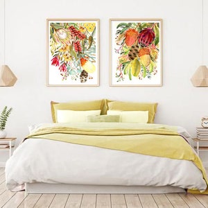 Puede incluir: Dos acuarelas enmarcadas de arreglos florales con flores rojas, amarillas y verdes. Las pinturas est&aacute;n colgadas en una pared blanca sobre una colcha de cama amarilla.