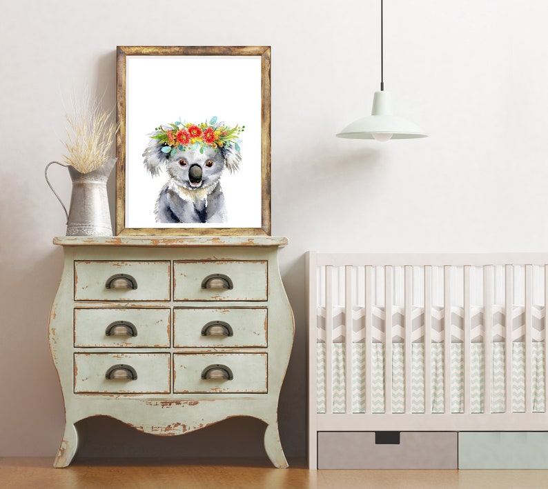 Puede incluir: Una pintura de acuarela de un koala con una corona de flores. El koala es gris y tiene la nariz y el pecho blancos. La corona est&aacute; hecha de flores rojas, naranjas y amarillas. La pintura est&aacute; enmarcada en un marco de madera r&uacute;stico y est&aacute; colgada en una pared blanca.