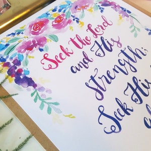 May include: Watercolor floral print with the text "Seek the Lord and His strength; Seek His face always" in a blue and purple calligraphy font.