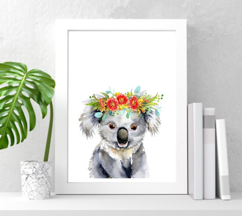 Puede incluir: Una pintura de acuarela de un koala con una corona de flores. El koala es gris y tiene una expresi&oacute;n linda. Las flores de la corona son rojas, amarillas y azules.