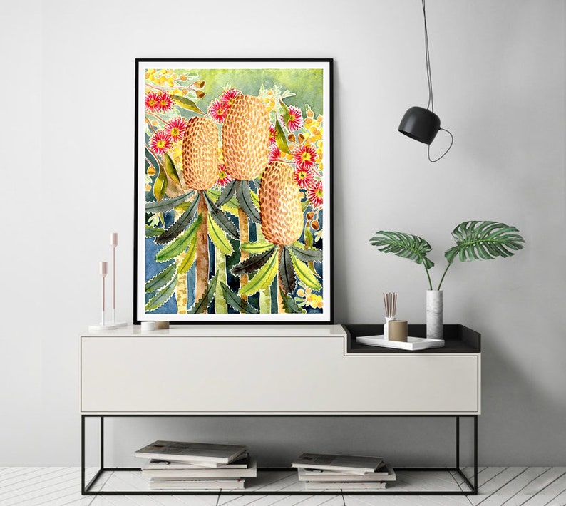 Puede incluir: Pintura acuarela de un grupo de flores de Banksia amarillas y rojas con hojas verdes sobre un fondo azul.