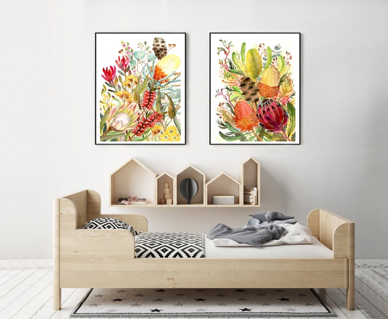 Puede incluir: Dos pinturas al agua enmarcadas de coloridas flores nativas australianas, incluyendo tonos rojos, amarillos y verdes. Las pinturas se exhiben sobre una cama de madera con un colch&oacute;n blanco y ropa de cama con estampado blanco y negro.
