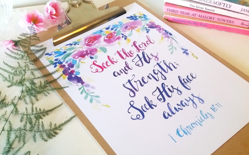 May include: A watercolor print with a floral design in shades of pink, blue, and purple. The print features the text "Seek the Lord and His Strength: Seek His face always" and the scripture reference "1 Chronicles 16:11".