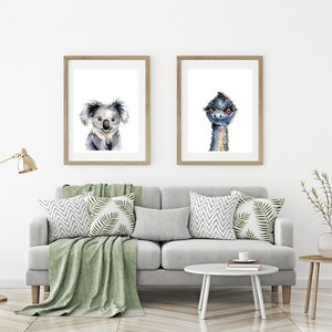 May include: Two framed watercolor paintings of animals. The left painting features a koala with a light gray fur and brown eyes. The right painting features an emu with a blue-gray head and neck and orange eyes.