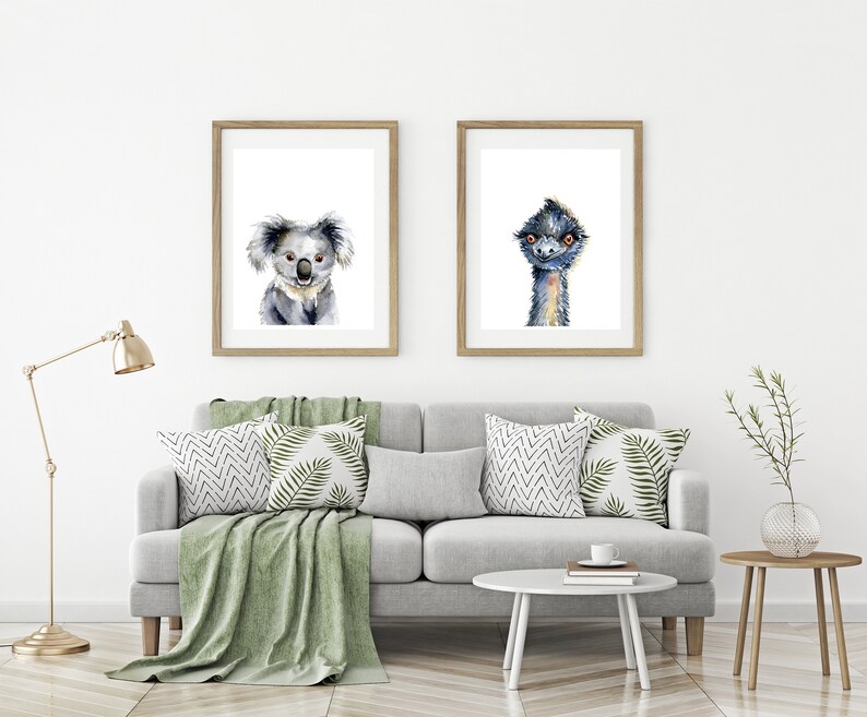 May include: Two framed watercolor paintings of animals. The left painting features a koala with a light gray fur and brown eyes. The right painting features an emu with a blue-gray head and neck and orange eyes.