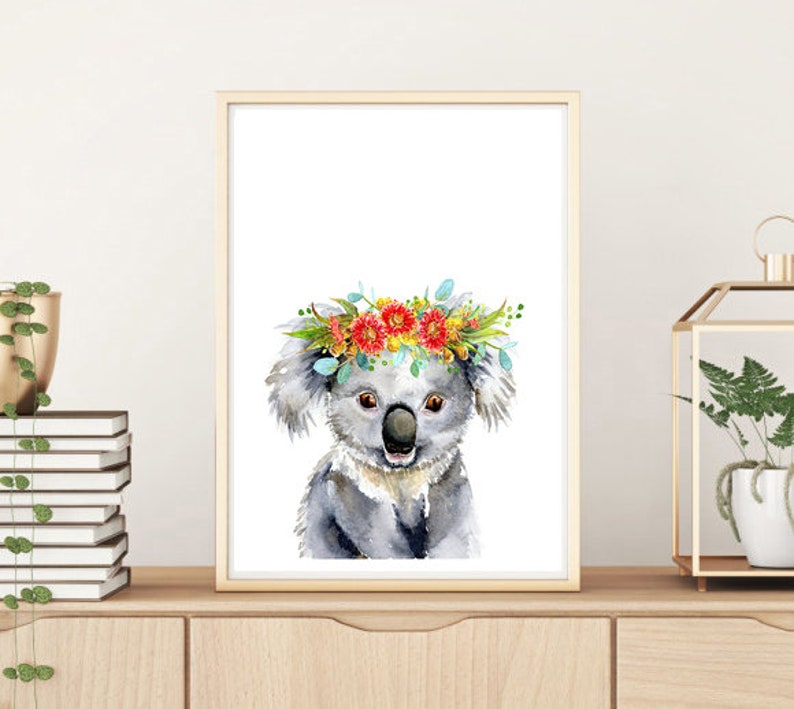 Puede incluir: Una pintura de acuarela de un koala con una corona de flores. El koala es gris y tiene la nariz negra. La corona de flores est&aacute; hecha de flores rojas, amarillas y naranjas.