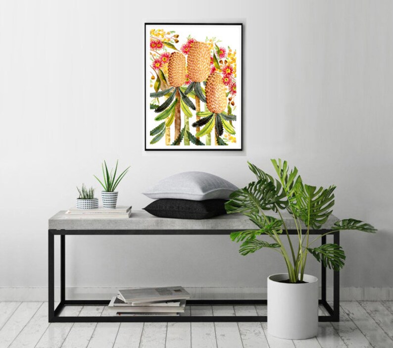 Puede incluir: Una pintura de acuarela enmarcada de tres flores de Banksia amarillas y rosadas con hojas verdes sobre un fondo blanco.