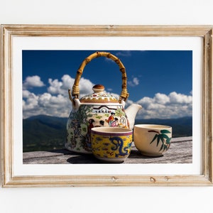May include: A framed print featuring a ceramic teapot with a bamboo handle and colorful painted figures, accompanied by two small tea cups. One cup is yellow with a blue dragon motif, and the other is cream-colored with green bamboo leaf designs.