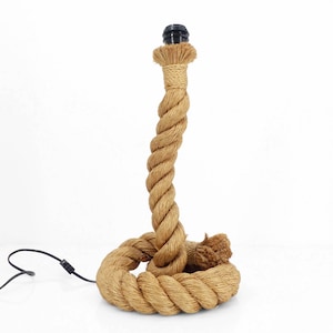 May include: A decorative table lamp made from thick, twisted rope. The lamp features a brown rope base and a spiraling rope column, topped with a black bulb socket. A black power cord extends from the base. The lamp is designed to sit on a flat surface.