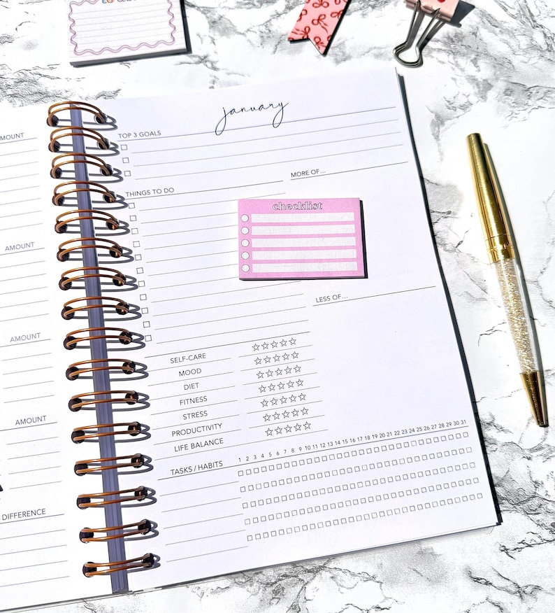 May include: Open spiral-bound planner with a gold pen. The planner is open to a page labeled "January" with sections for goals, tasks, and habits. A pink checklist sticky note is attached.