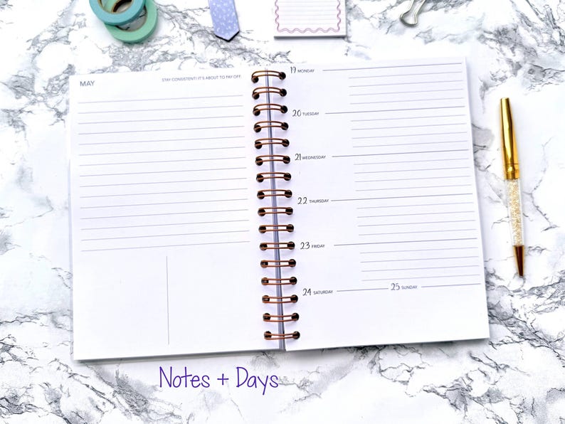 May include: Open spiral-bound planner with lined pages, featuring the month of May and daily sections from Monday to Sunday. A gold pen with a crystal-like barrel rests on the side. The words "Notes + Days" are at the bottom.