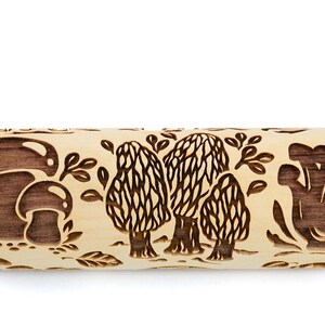May include: A wooden rolling pin with a brown mushroom design. The rolling pin has a light brown wood color and features three different mushroom designs, including a cluster of mushrooms, a single mushroom, and a group of three mushrooms.