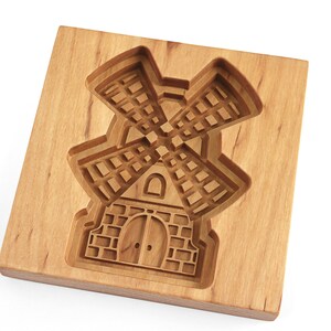 Puede incluir: Un cortador de galletas de madera con forma de molino de viento. El cortador tiene un dise&ntilde;o detallado con una base de ladrillo y un molino de viento con aspas.