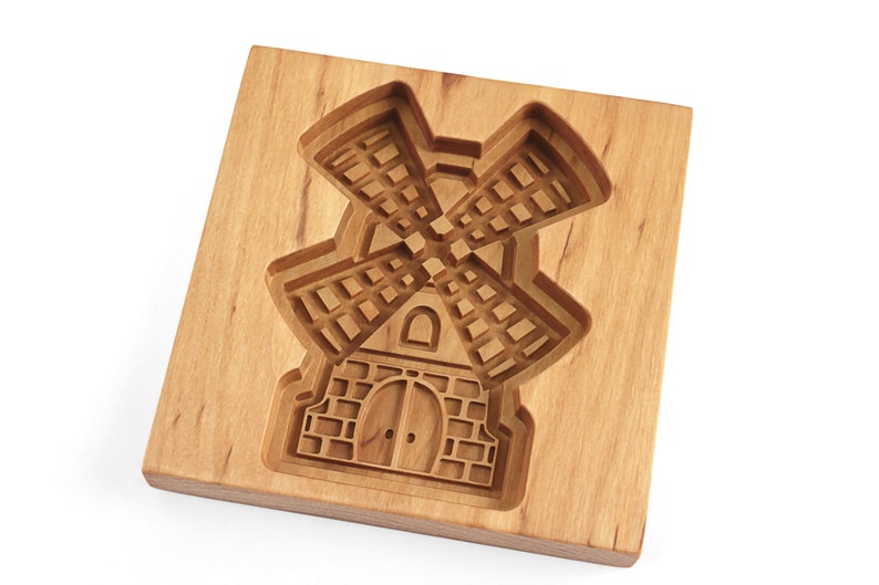 Puede incluir: Un cortador de galletas de madera con forma de molino de viento. El cortador tiene un dise&ntilde;o detallado con una base de ladrillo y un molino de viento con aspas.