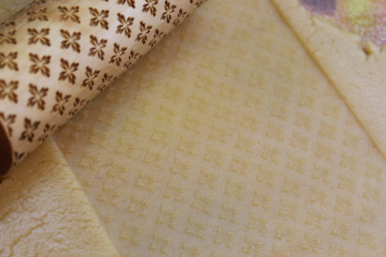 May include: A close-up of a wooden rolling pin with a snowflake pattern. The rolling pin is being used to roll out dough, which is imprinted with the snowflake pattern.