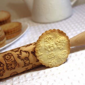 May include: A wooden rolling pin with a design of cartoon characters. The rolling pin is used to create cookies with the same design. A cookie with the design is shown on the rolling pin.