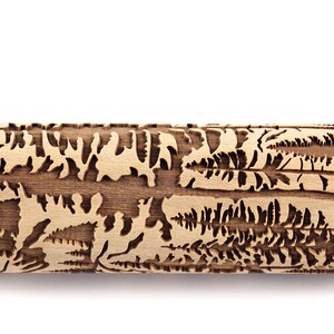 May include: A wooden rolling pin with a detailed forest scene carved into its surface. The design includes trees, ferns, and other foliage, creating a textured pattern for baking. The rolling pin is made of light-colored wood.