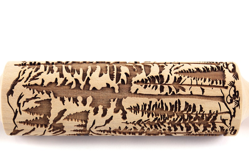 May include: A wooden rolling pin with a detailed forest scene carved into its surface. The design includes trees, ferns, and other foliage, creating a textured pattern for baking. The rolling pin is made of light-colored wood.