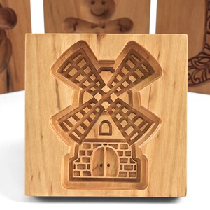 Puede incluir: Cortador de galletas de madera con forma de molino de viento. El cortador est&aacute; hecho de madera marr&oacute;n claro y tiene un dise&ntilde;o detallado.