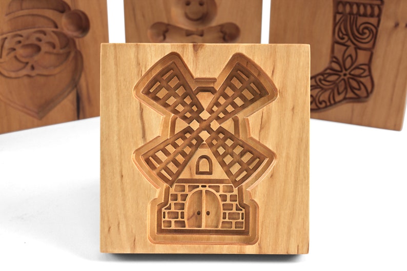 Puede incluir: Cortador de galletas de madera con forma de molino de viento. El cortador est&aacute; hecho de madera marr&oacute;n claro y tiene un dise&ntilde;o detallado.