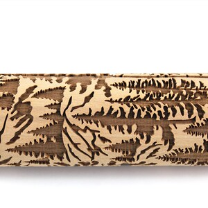May include: A wooden rolling pin with a detailed forest scene carved into its surface. The design features trees and foliage, creating a textured pattern. The rolling pin is light brown with a natural wood grain.