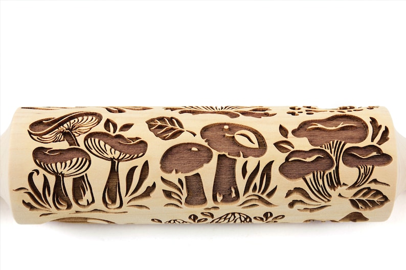 May include: A wooden rolling pin with a carved design of mushrooms and leaves. The rolling pin is light brown with dark brown carvings.