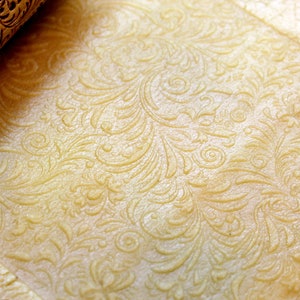 May include: A close-up of a rolling pin with a decorative pattern being used to roll out dough. The dough is imprinted with the pattern from the rolling pin, creating a decorative design.