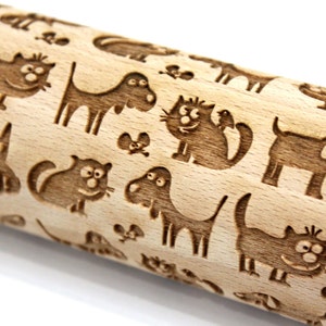 May include: A wooden rolling pin with a repeating pattern of cats and dogs engraved on the surface. The animals are cartoon-like and have simple features.