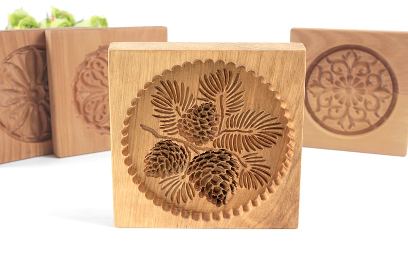 Puede incluir: Cuatro cortadores de galletas de madera, cada uno con un dise&ntilde;o diferente. El cortador del centro presenta un dise&ntilde;o de pi&ntilde;a y agujas de pino. Los otros cortadores presentan un dise&ntilde;o floral.