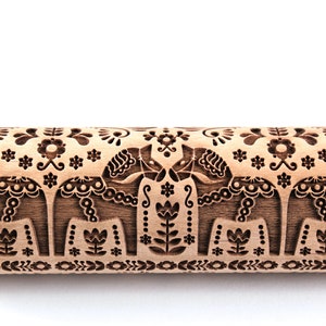 Op de afbeelding: Een houten deegroller met een gesneden ontwerp van twee Dala-paarden die elkaar aankijken. Het ontwerp bevat traditionele Zweedse volkskunstmotieven, zoals bloemen, bladeren en geometrische patronen.