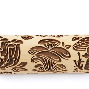 May include: A wooden rolling pin with a carved design of mushrooms and leaves. The rolling pin is made of natural wood and has a light brown color.