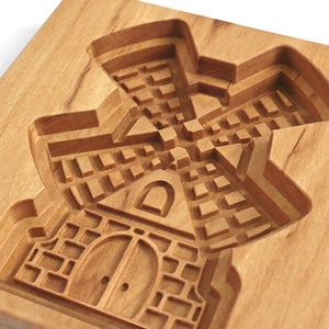 Puede incluir: Un cortador de galletas de madera con forma de molino de viento. El cortador tiene un dise&ntilde;o detallado con una base de ladrillo, una puerta y una ventana.