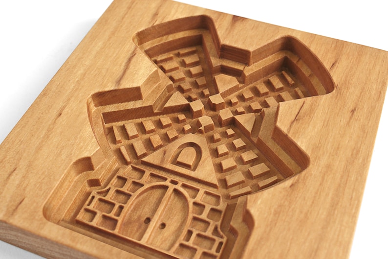 Puede incluir: Un cortador de galletas de madera con forma de molino de viento. El cortador tiene un dise&ntilde;o detallado con una base de ladrillo, una puerta y una ventana.