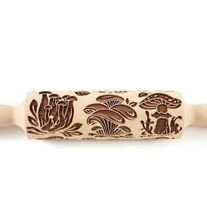 May include: A wooden rolling pin with a carved design of mushrooms. The rolling pin is light brown and has a natural wood finish.