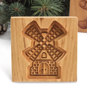 Puede incluir: Un cortador de galletas de madera con forma de molino de viento. El cortador est&aacute; hecho de madera marr&oacute;n claro y tiene un dise&ntilde;o detallado.