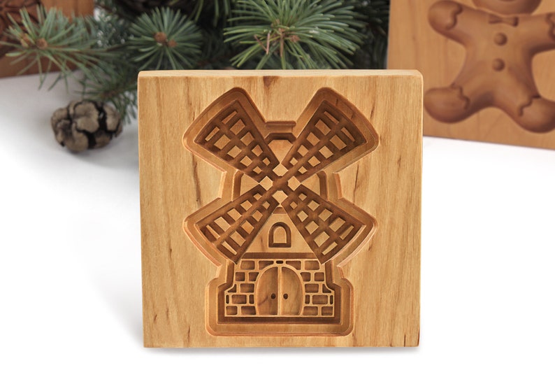 Puede incluir: Un cortador de galletas de madera con forma de molino de viento. El cortador est&aacute; hecho de madera marr&oacute;n claro y tiene un dise&ntilde;o detallado.