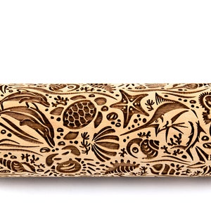 May include: A wooden rolling pin with an engraved sea life design. The design includes dolphins, sea turtles, starfish, fish, seashells, and a jellyfish. The rolling pin is light brown in color and is set against a white background.