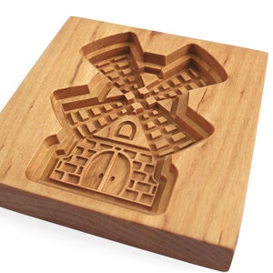 Puede incluir: Un cortador de galletas de madera con forma de molino de viento. El cortador tiene un dise&ntilde;o detallado con una puerta y ventanas.