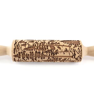 May include: A wooden rolling pin with a detailed forest pattern carved into the rolling surface. The handles are smooth and light-colored, contrasting with the darker, textured design of the rolling surface. Ideal for baking.