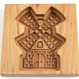 Puede incluir: Un cortador de galletas de madera con forma de molino de viento. El cortador tiene un dise&ntilde;o detallado con una base de ladrillo y un molino de viento con aspas.