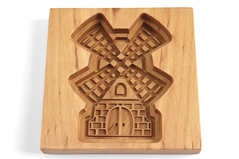 Puede incluir: Un cortador de galletas de madera con forma de molino de viento. El cortador tiene un dise&ntilde;o detallado con una base de ladrillo y un molino de viento con aspas.
