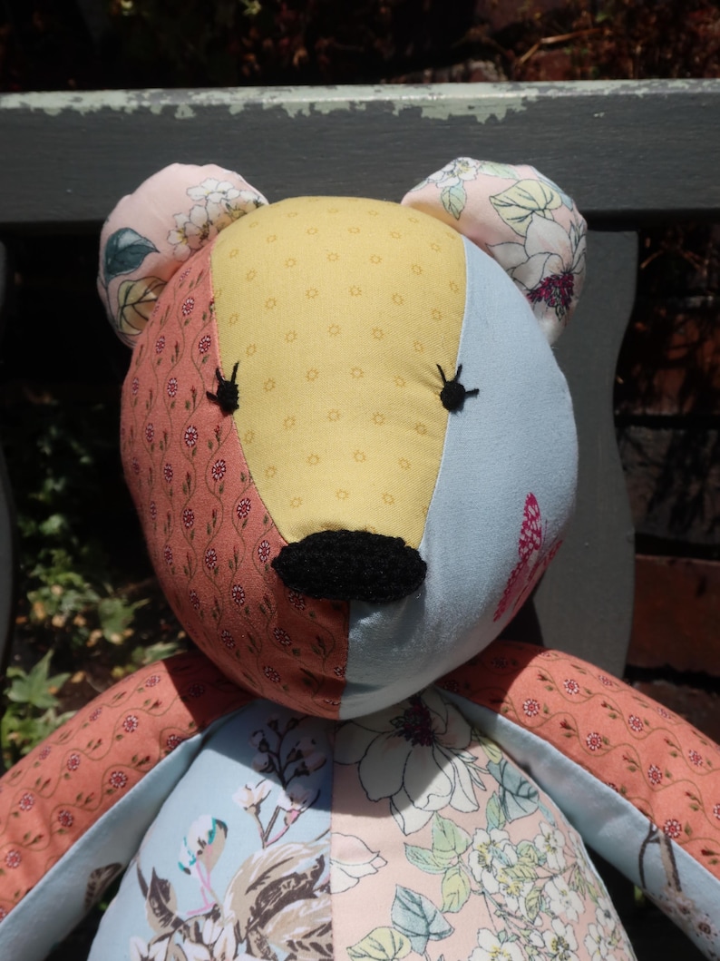 May include: A handmade patchwork teddy bear with a yellow, light blue, and floral patterned face. The bear has black embroidered eyes and nose, and pink floral ears. The bear's arms and body are also made of floral patterned fabric.
