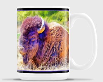 May include: White ceramic mug featuring a watercolor painting of a bison. The bison has brown fur, a purple face, and yellow horns. The mug has a black and purple border.