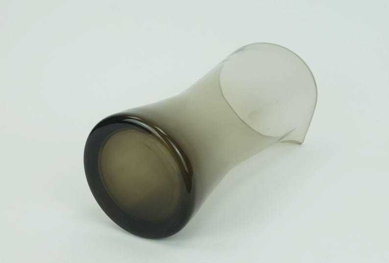 May include: A smoked glass pitcher with a wide base and a narrow opening. The pitcher is made of clear glass with a smoky gray tint.