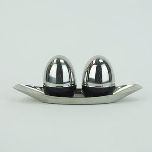 Può includere: Un moderno set di saliera e pepiera. Il set comprende due shaker a forma di uovo, in acciaio inossidabile, con basi nere, appoggiati su un vassoio in acciaio inossidabile abbinato.