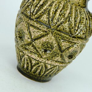 May include: A green ceramic pitcher with a geometric pattern. The pitcher has a textured surface and a wide mouth.