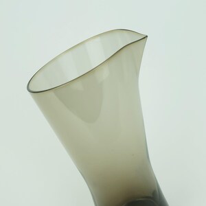May include: A clear glass pitcher with a brown tint. The pitcher has a wide mouth and a narrow base.