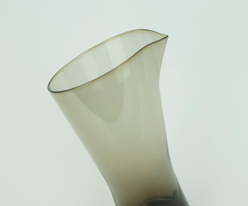 May include: A clear glass pitcher with a brown tint. The pitcher has a wide mouth and a narrow base.